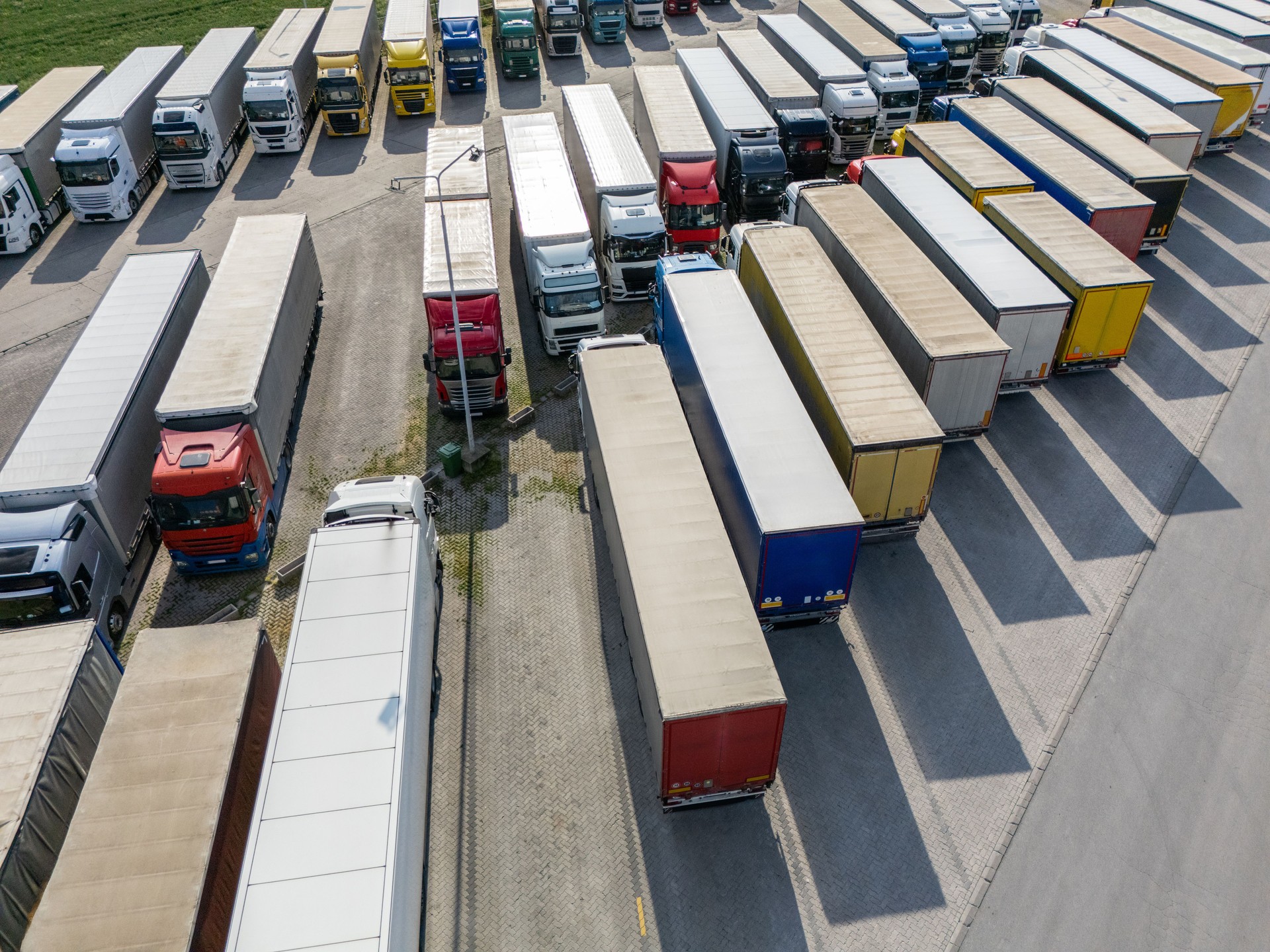 Aerial view of a large truck parking lot at a logistics hub, with multiple commercial semi trucks parked in organized rows.